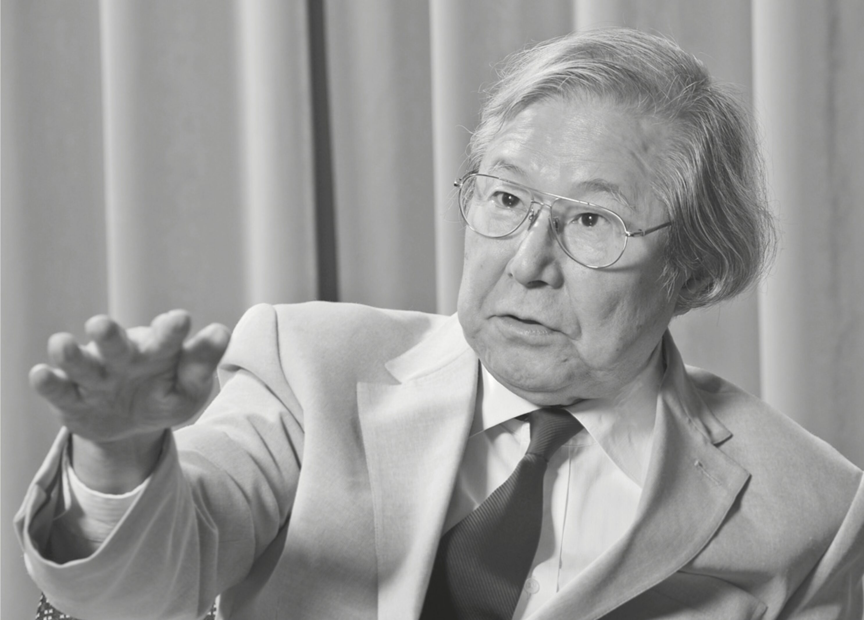 A black-and-white photo of mathematician Heisuke Hironaka looking to the side of the camera and gesturing with his right hand.