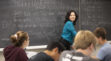 Harvard math professor Lauren Williams teaching a class and writing math formulas in chalk on a blackboard.