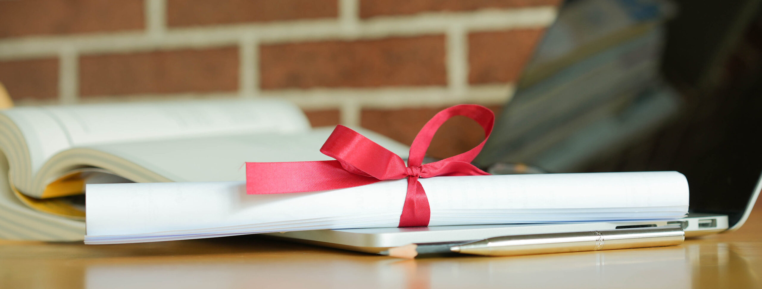 A rolled up piece of paper tied with a red ribbon on a desk.