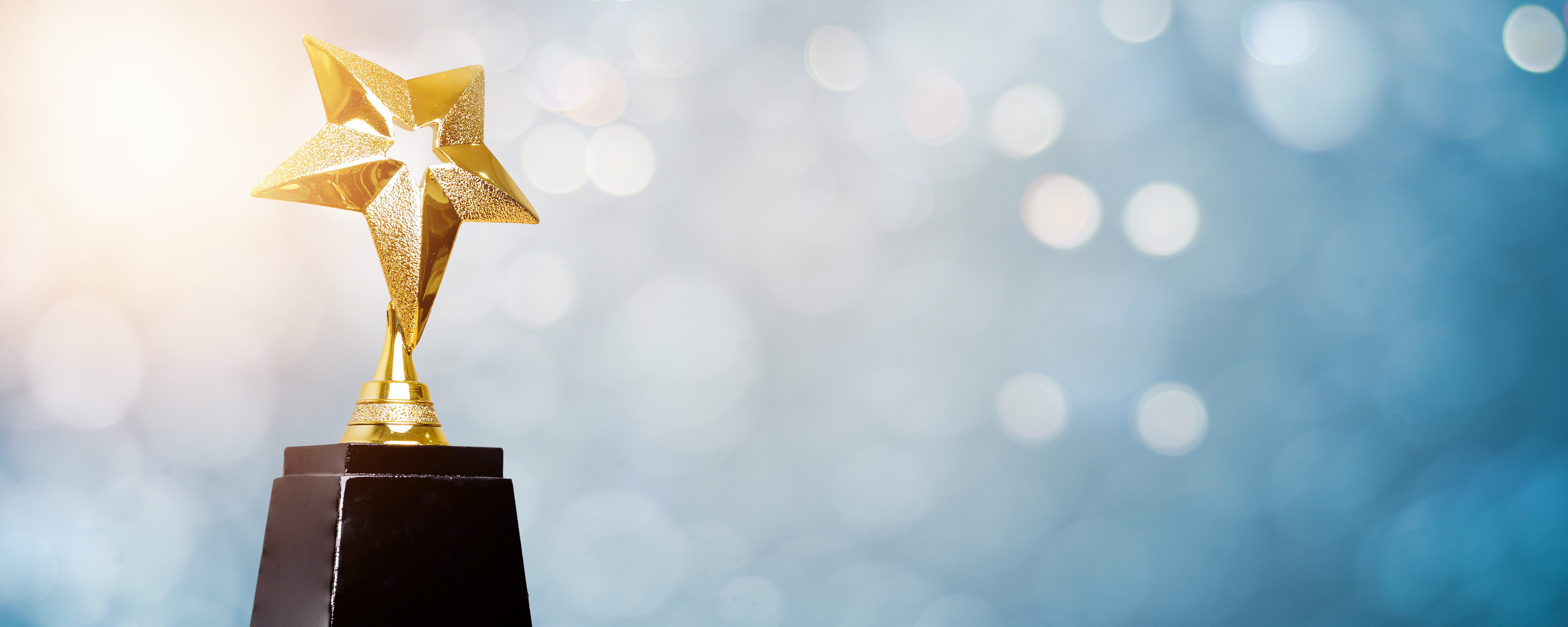 Golden star award on a black pedestal in front of blurred light flares on a blue background.